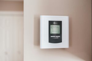 A family adjusting a smart thermostat — a device that learns their habits and controls heating automatically — in a cosy, modern living room with an Eluxevo infrared panel on the wall.