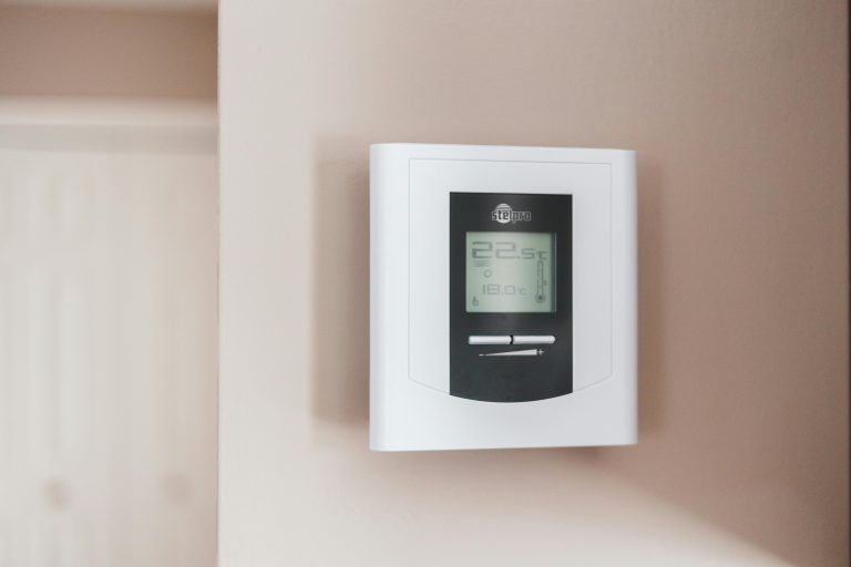 A family adjusting a smart thermostat — a device that learns their habits and controls heating automatically — in a cosy, modern living room with an Eluxevo infrared panel on the wall.